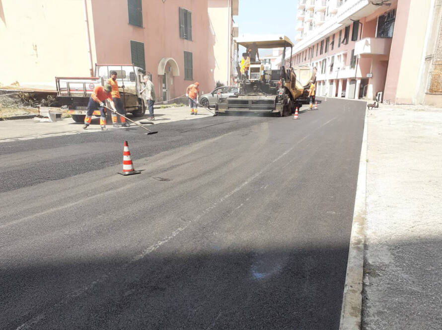 Operai e mezzi meccanici di ASTER Genova durante i lavori di stesa del nuovo asfalto su una strada cittadina